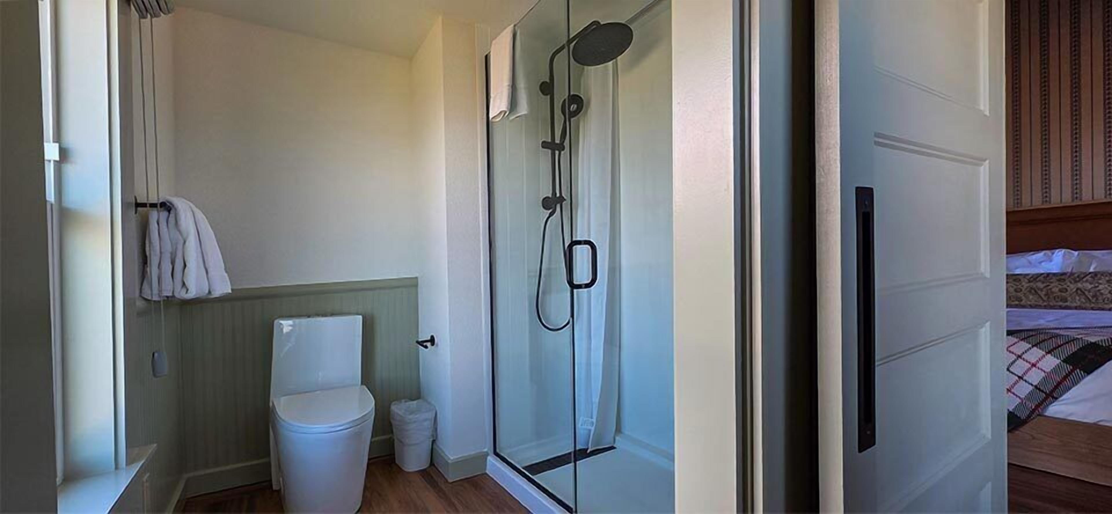 A compact bathroom with a toilet, a small trash bin, and a glass shower enclosure.