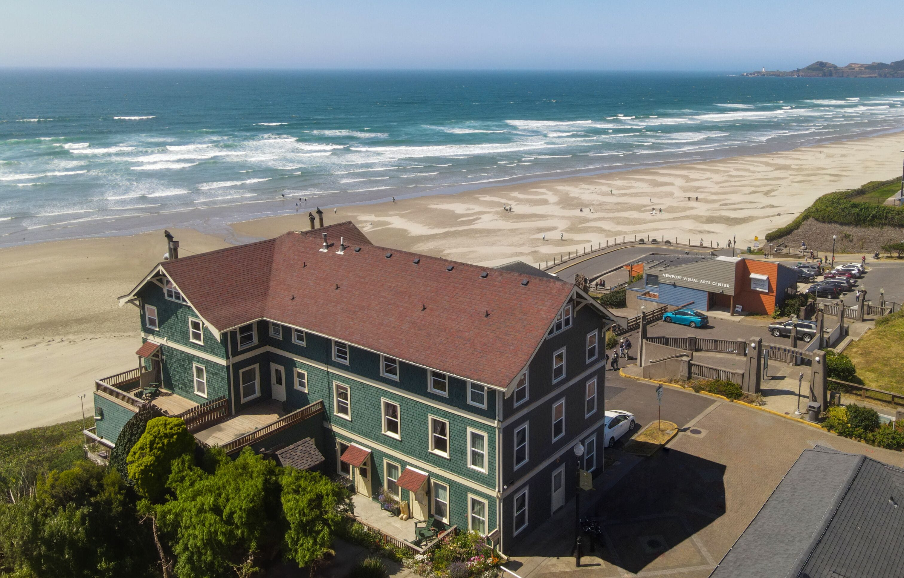A coastal building with a red roof, adjacent to a beach with waves and a clear sky.