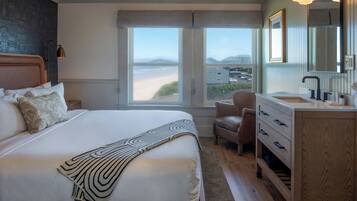 A bedroom with a large bed, a view of the beach, a chair, and a wooden dresser with drawers.