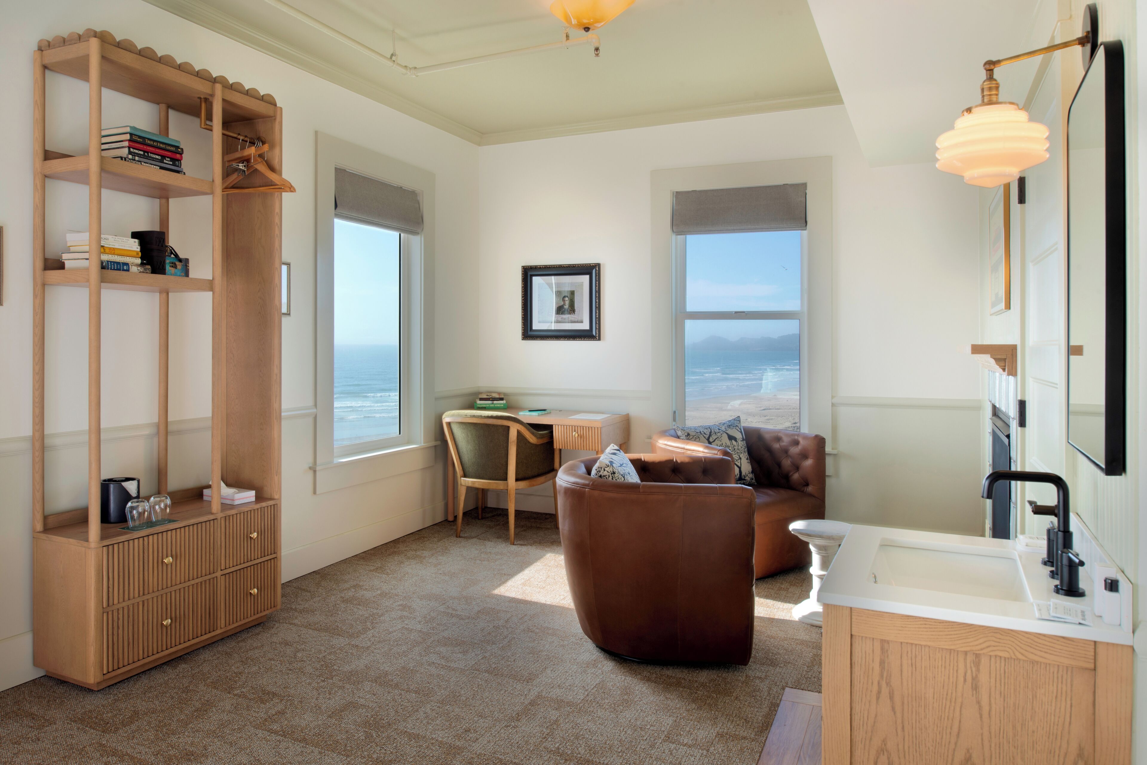 Una habitación con una estantería de madera, un sofá de cuero marrón, una mesita y vistas al océano a través de amplios ventanales.