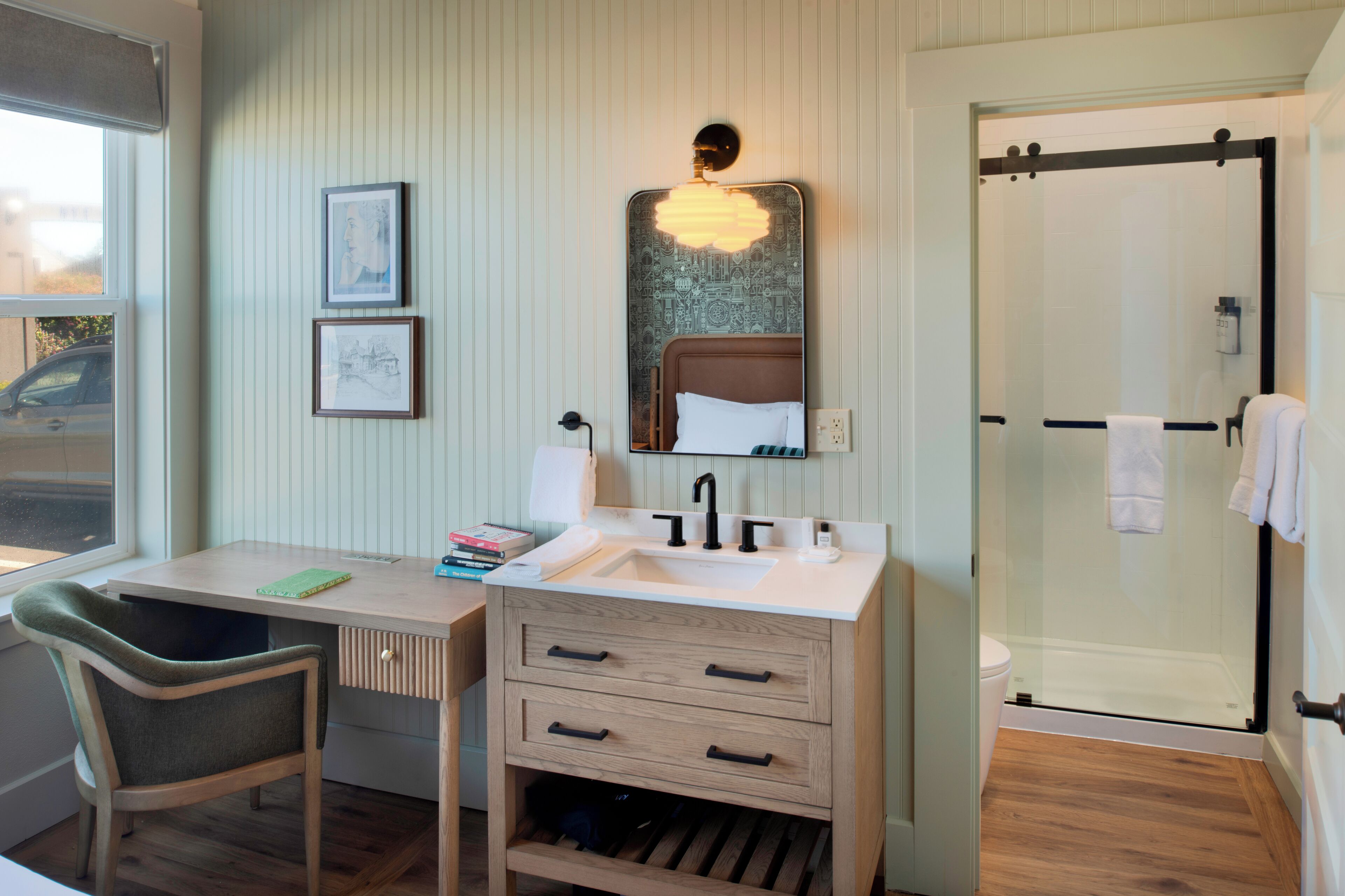 A bathroom with a shower, a sink, a mirror, and a chair.