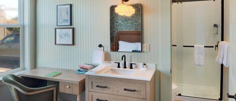 A bathroom with a shower, a sink, a mirror, and a chair.