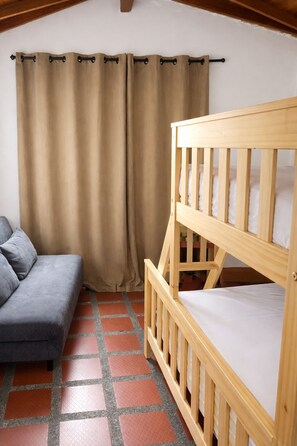Habitació amb un llit superposat de fusta, un sofà gris i una cortina.