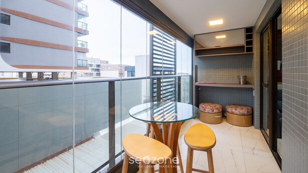 A balcony with a glass table and two chairs, a small seating area with stools, and a view of buildings. - 1 Bedroom Apart w/ Air 120m From the Beach Esb0310 (Salvador)