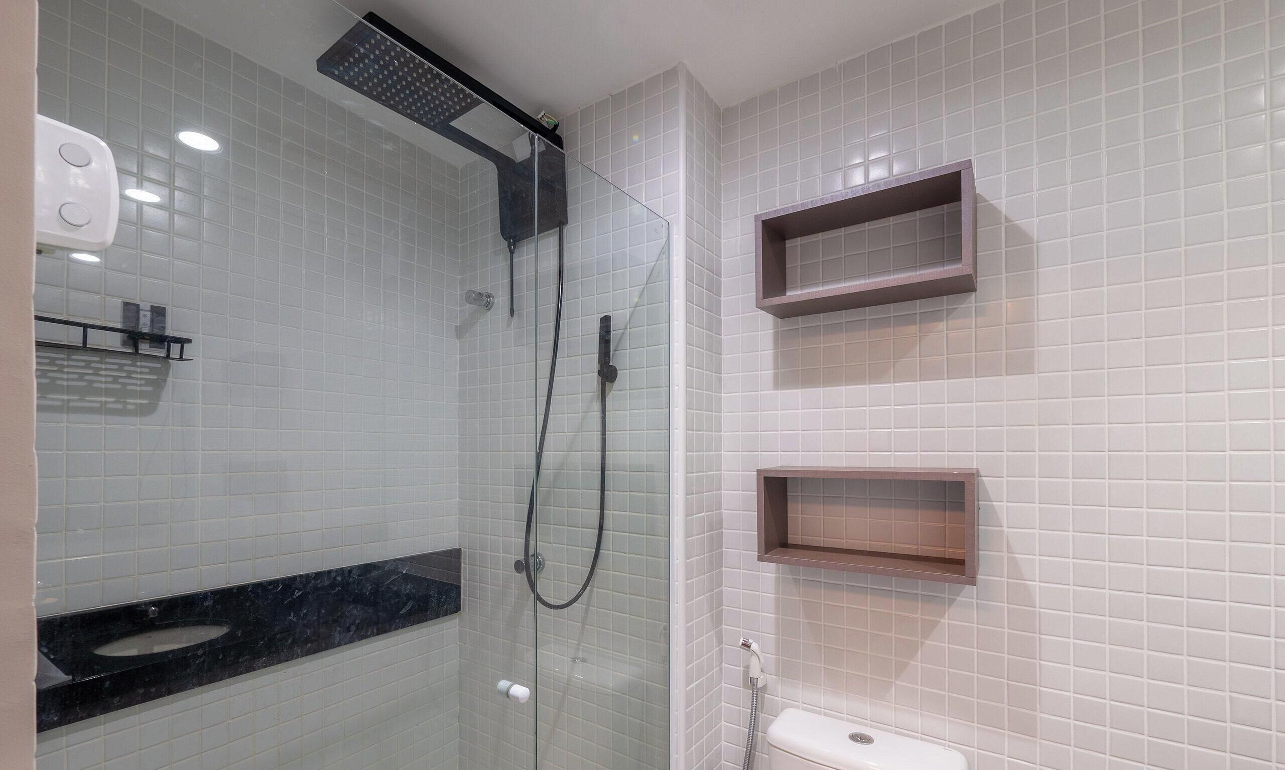 Un baño moderno con cabina de ducha de vidrio, encimera de mármol negro y paredes cubiertas de azulejos blancos.