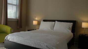 Habitación de hotel con una cama grande, dos lámparas de noche, una mesita de noche, un sillón verde y una ventana con persianas.