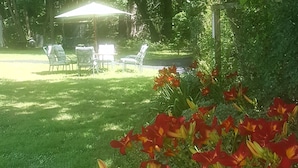 Un jardín con césped y una mesa con sillas bajo una pérgola.