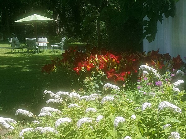 Een tuin met gazon, een tafel met stoelen en diverse bloemen.