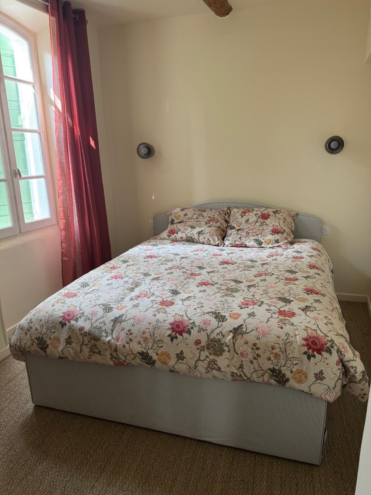 A bedroom with a bed, floral bedding, a window with curtains, and a ceiling fan.