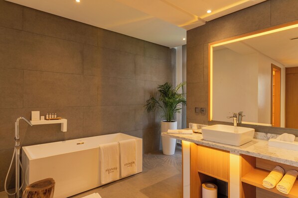 A modern bathroom with a large bathtub, a sink, and a mirror. There is a shelf with toiletries and a potted plant. - NOMMOS Beach RESORT & POOL CLUB (Marrakech)