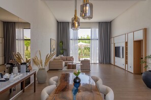 A spacious living area with a wooden coffee table, sofas, and a TV on a wooden cabinet. - NOMMOS Beach RESORT & POOL CLUB (Marrakech)