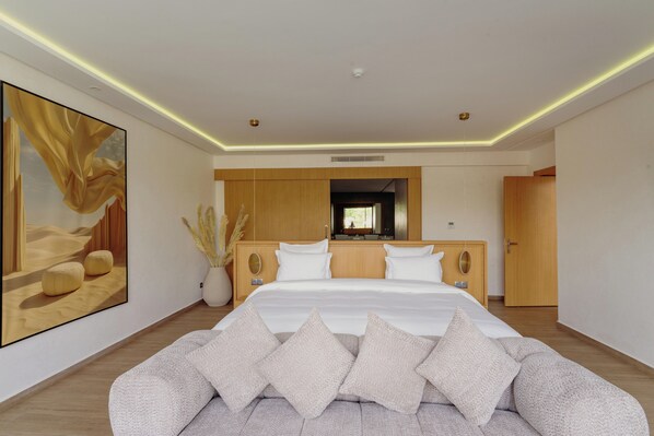 A modern bedroom with a large bed, a sofa, and a large framed artwork on the wall. - NOMMOS Beach RESORT & POOL CLUB (Marrakech)