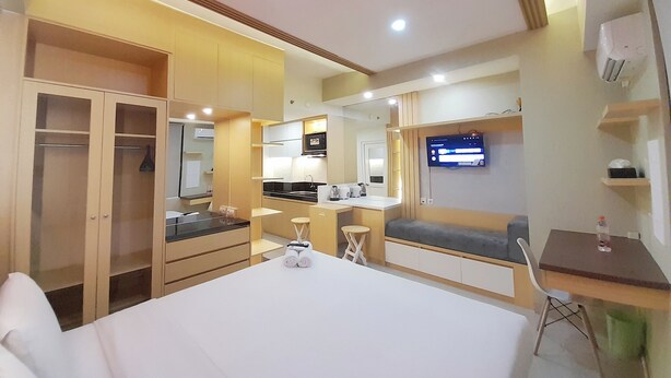 A hotel room with a bed, a desk, a chair, a TV, a kitchenette, and a wardrobe.