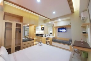 Une chambre d’hôtel comprenant un lit, un bureau, une chaise, une télévision, un coin cuisine et une armoire.
