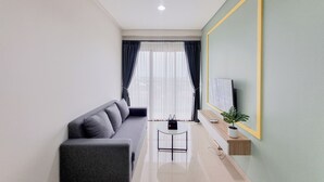 A modern living room with a sofa, a small table, a TV, and a large mirror. - Simply Look 1Br Apartment Patraland Amarta (Ngaglik)