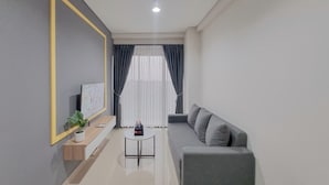 Una sala de estar moderna con un sofá gris, una pequeña mesa redonda de centro, un televisor sobre un soporte de madera y una planta en maceta.