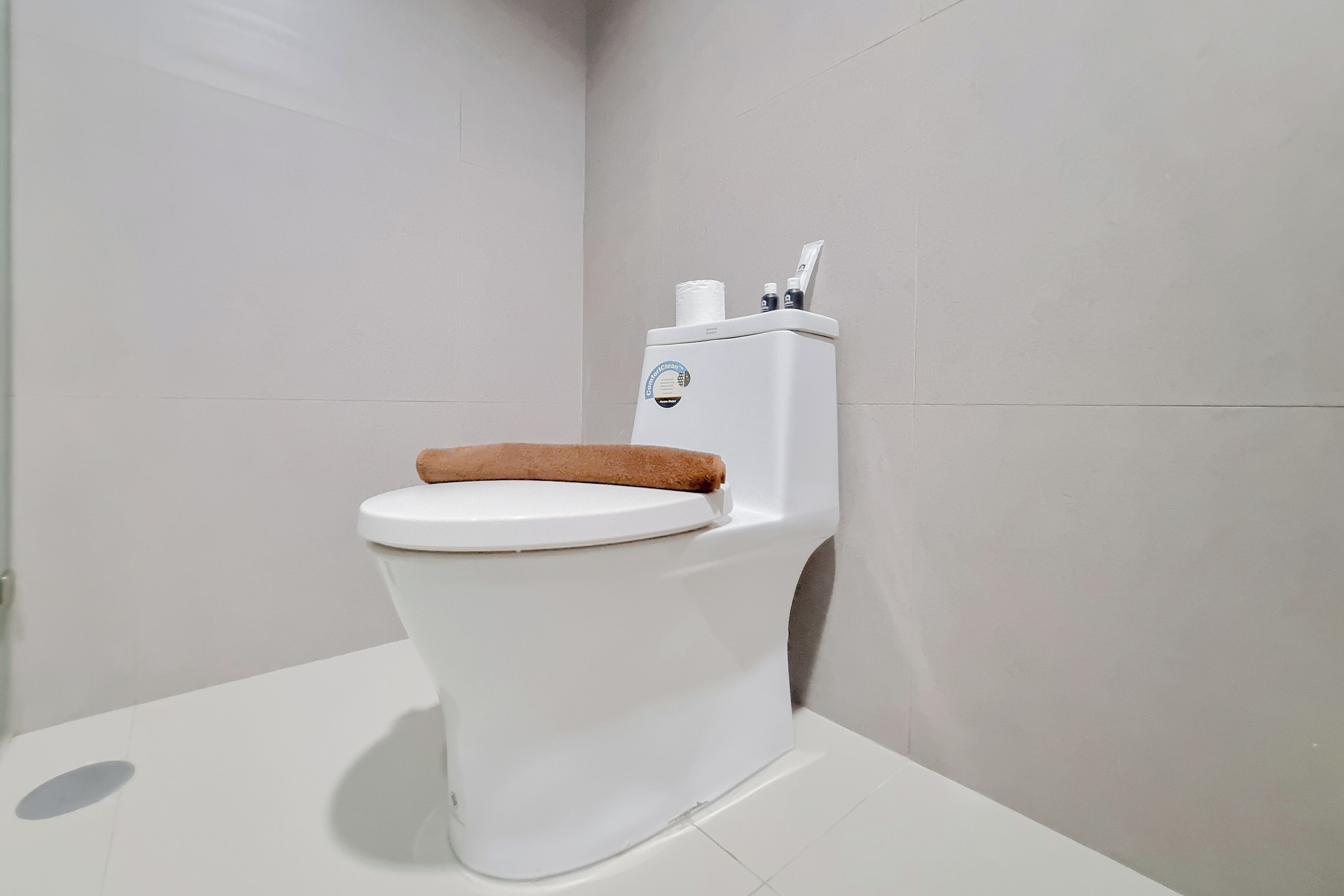 Des toilettes blanches avec un abattant marron et un réservoir d’eau doté d’une poignée de chasse d’eau.