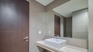 Ein Badezimmer mit einem weißen Waschbecken, einem großen Spiegel und einer dunkelbraunen Tür.
