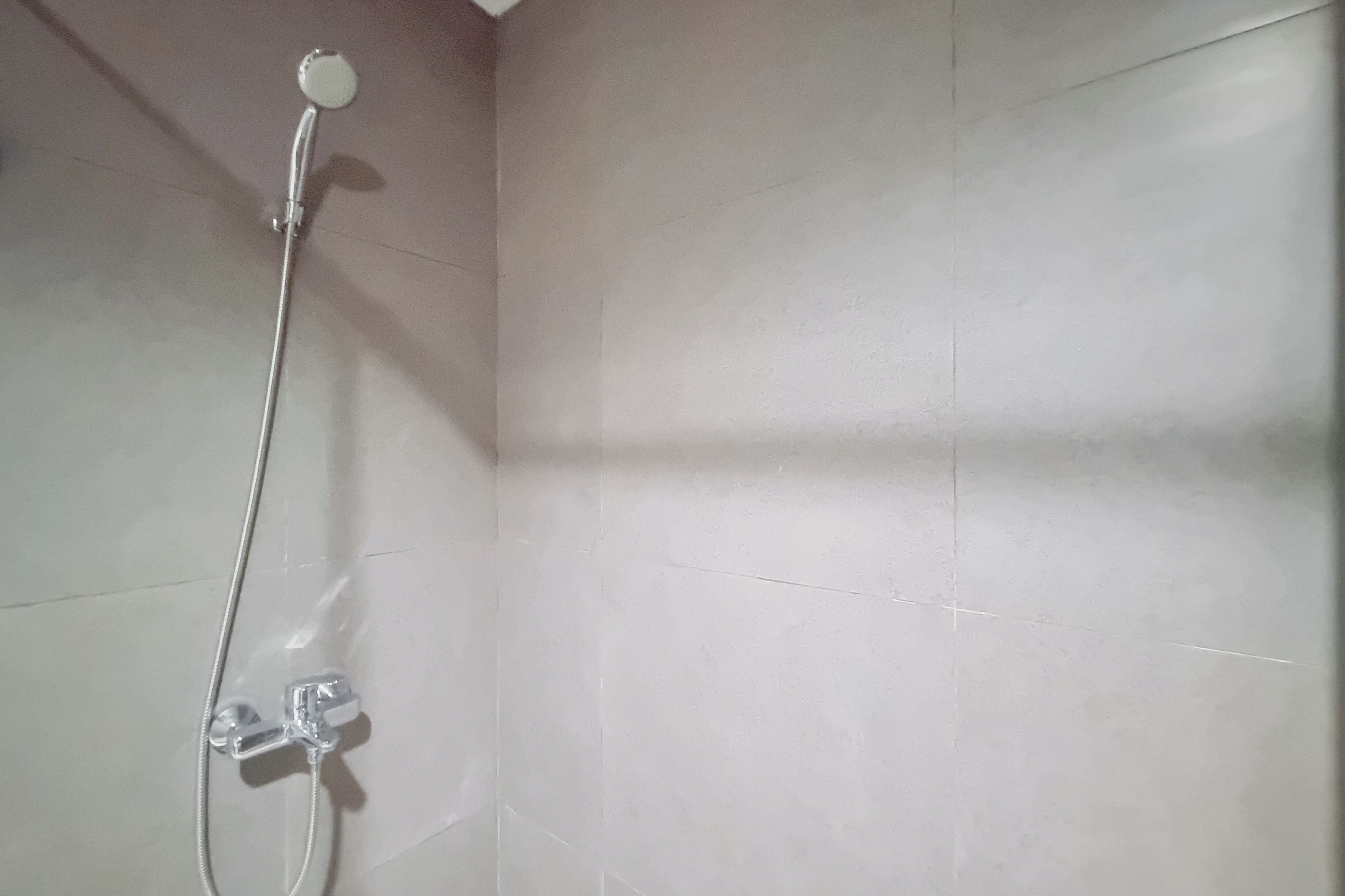 A shower area with a handheld showerhead and a wall-mounted faucet.