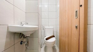 A bathroom with a white sink, toilet, and wooden door. - Simple Studio (No Kitchen) Bandaraya - Tallasa City Makassar Apartment (Makassar)