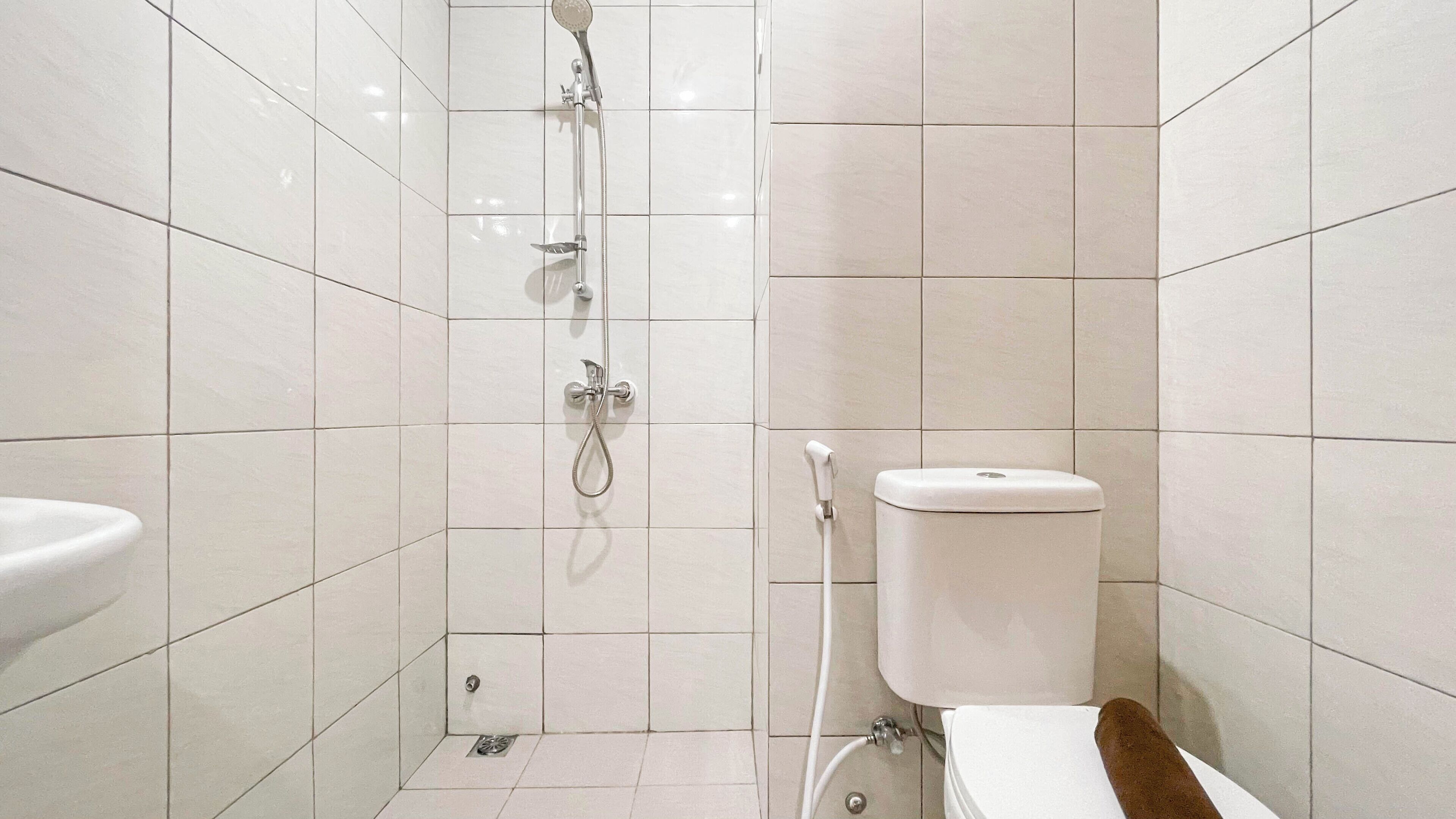 A small, modern bathroom with white tiles, a toilet, a shower, and a sink.