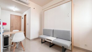 A modern room with a grey sofa, a wooden desk, and a white chair. - Studio (No Kitchen) Apartment Near Unhas At Bandaraya - Tallasa City Makassar (Makassar)