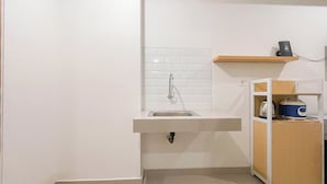 A compact kitchen with a built-in sink, white tiled backsplash, and a wooden shelf above the counter. - Studio (No Kitchen) Apartment Near Unhas At Bandaraya - Tallasa City Makassar (Makassar)