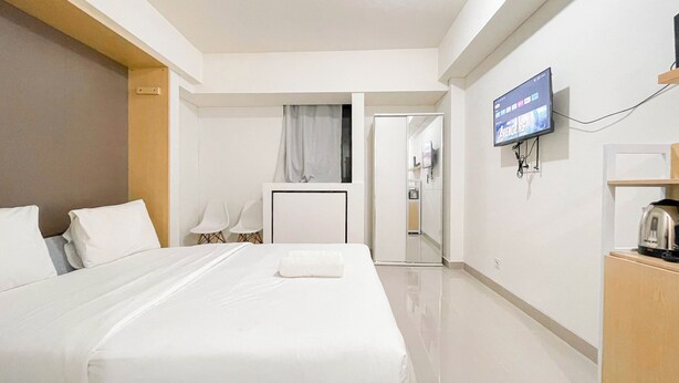 A hotel room with a bed, a TV mounted on the wall, a desk with a kettle, and a door leading to a bathroom. - Simple Look Studio (No Kitchen) Near Unhas Bandaraya - Tallasa City Makassar Apartment (Makassar)