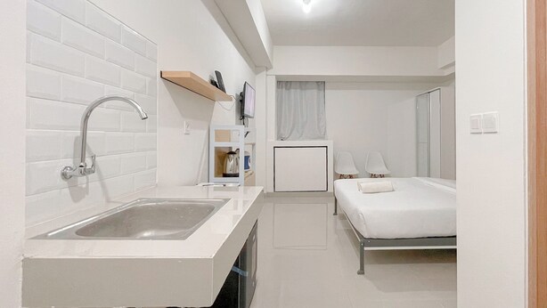 Una habitación de hotel moderna con un lavamanos blanco, una cama, una mesita de noche, un televisor y un armario pequeño.