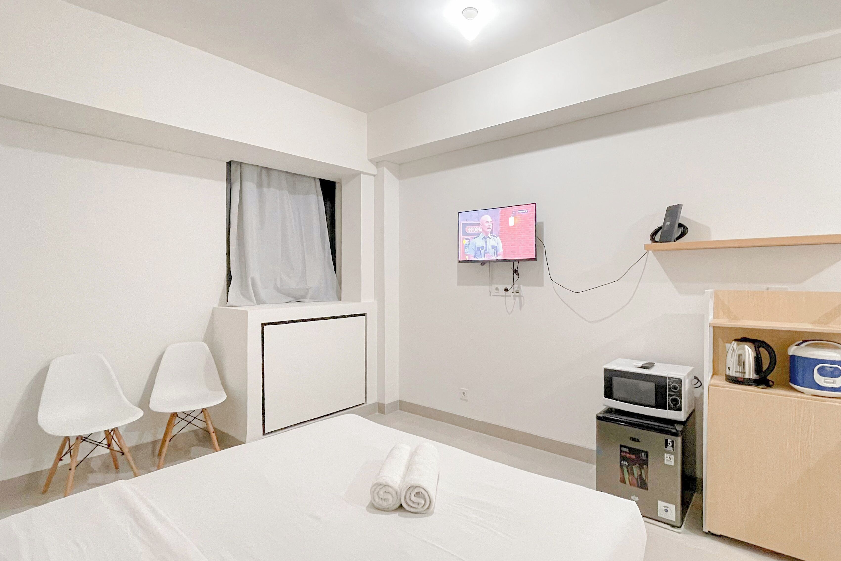 A hotel room with a bed, a TV mounted on the wall, a microwave, and a small kitchenette.