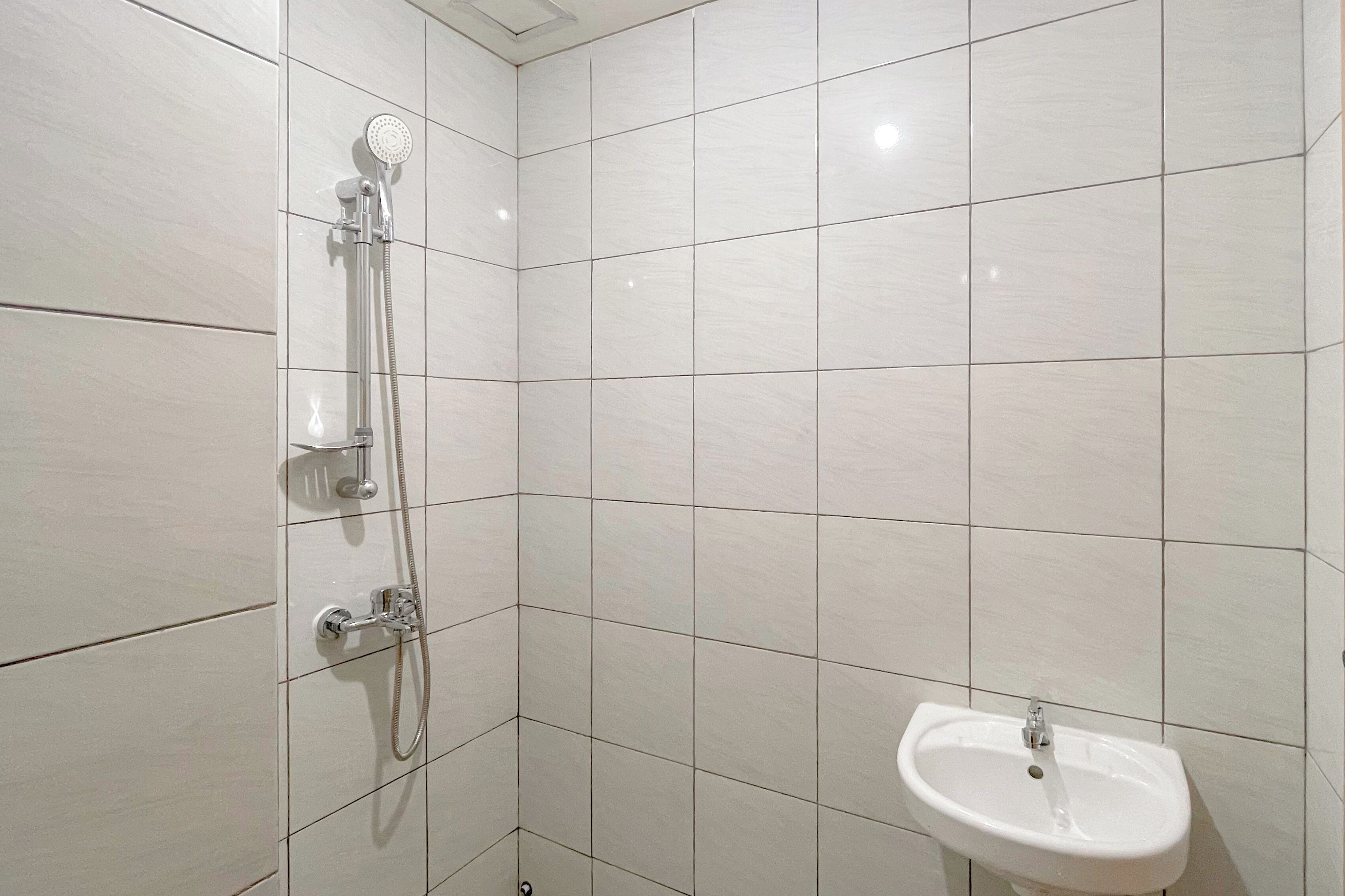 A bathroom with white tiled walls, a shower with a handheld showerhead, and a pedestal sink.