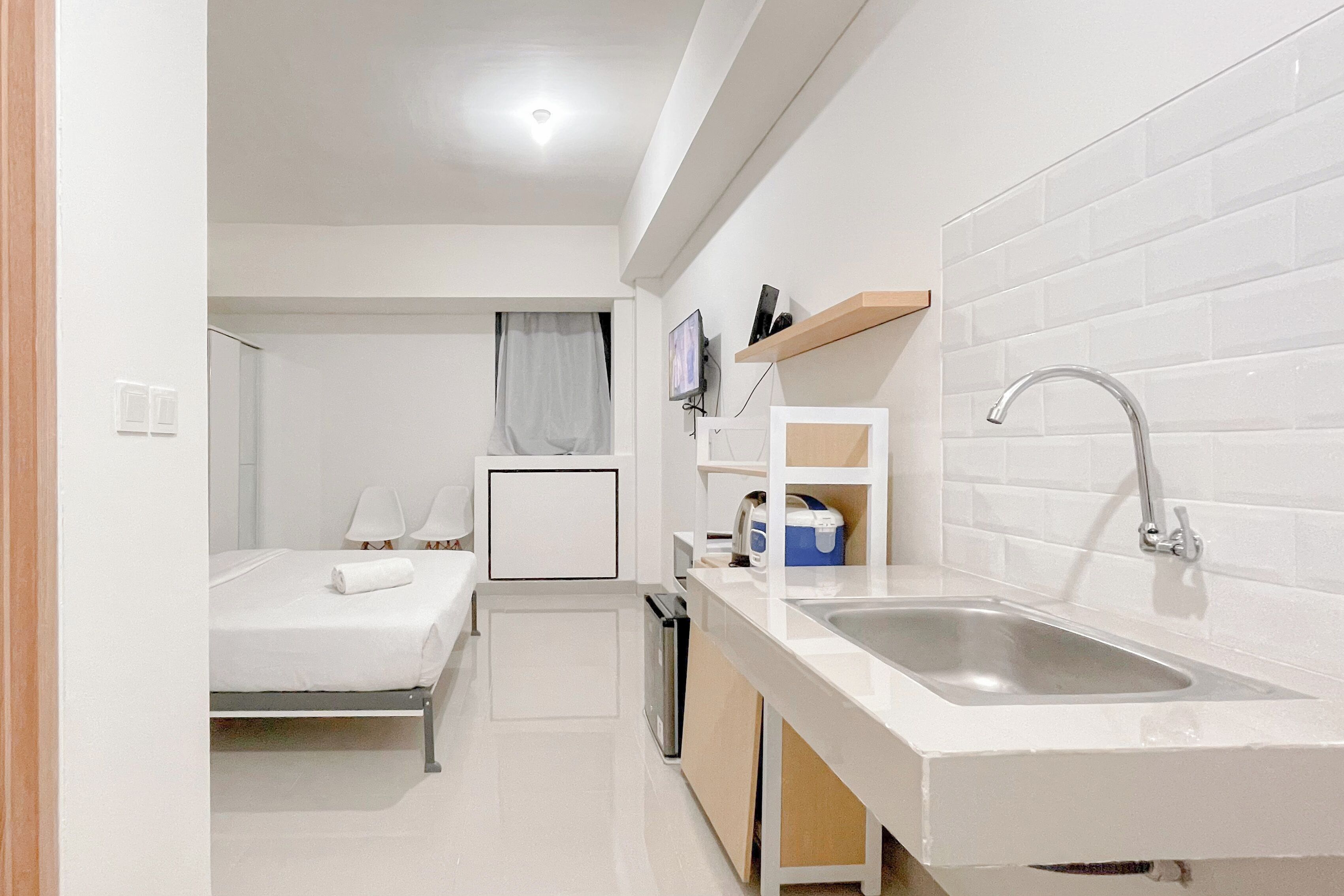 Quarto de hotel compacto com cozinha compacta, uma cama, televisão pequena e banheiro com pia e espelho.