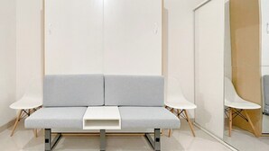 A modern room with a grey sofa, two white side tables, and a wooden wardrobe. - Simple Studio (No Kitchen) Bandaraya - Tallasa City Makassar Apartment Near Unhas (Makassar)