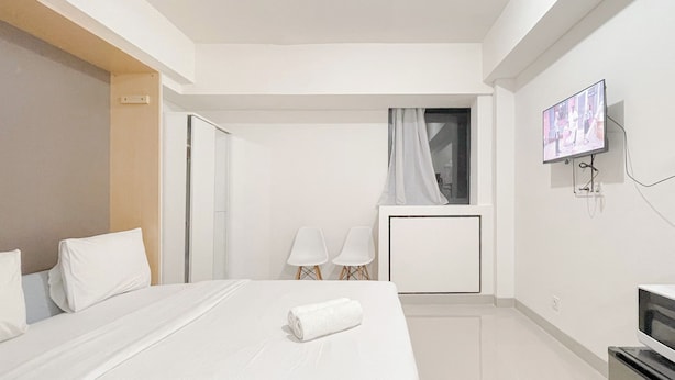 A hotel room with a bed, a TV, a desk, and a window with curtains. - Compact Studio (No Kitchen) At Bandaraya - Tallasa City Makassar Apartment (Makassar)