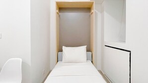 A narrow, walk-in closet with a bed at the end, a chair to the left, and a window on the right. - Neat Studio (No Kitchen) At Bandaraya - Tallasa City Makassar Apartment (Makassar)