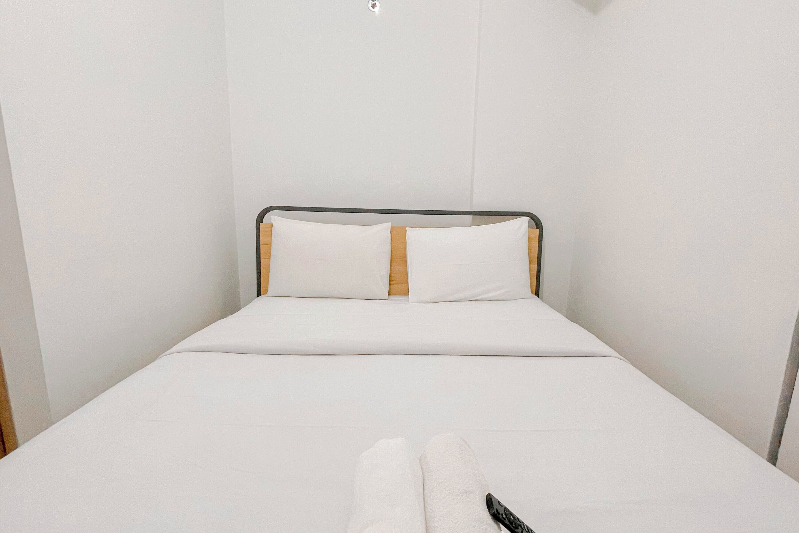 A single bed with white bedding and a wooden headboard in a room with white walls.