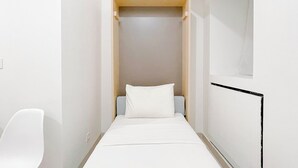 A narrow, modern room with a bed, a small seating area, and a window. - Good Deal Studio Room (No Kitchen) Bandaraya - Tallasa City Makassar Apartment (Makassar)