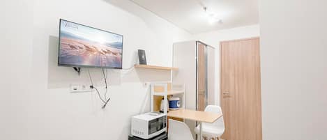 A compact room with a flat-screen TV mounted on the wall, a small table with chairs, a microwave, and a refrigerator.
