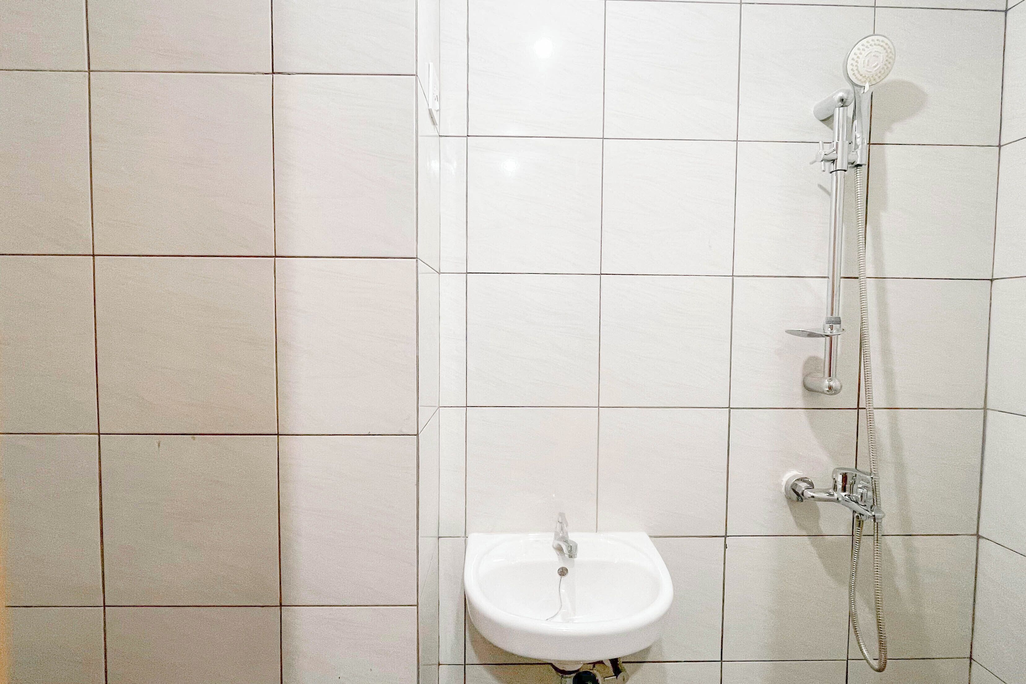 A bathroom with white tiles, a sink, and a shower with a handheld showerhead.