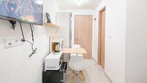 A small, modern room with a flat-screen TV mounted on the wall, a coffee maker, a white table, and a white chair. - Studio Apartment (No Kitchen) Near Unhas At Bandaraya - Tallasa City Makassar (Makassar)