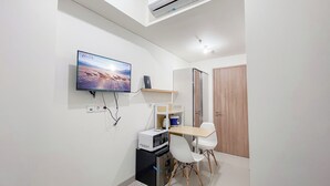 A modern room with a flat-screen TV mounted on the wall, a compact kitchenette with a microwave, a small refrigerator, and a wooden door.