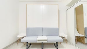 A modern waiting area with a grey sofa, two white side tables, and a small white table in front. - White Studio Room (No Kitchen) At Bandaraya - Tallasa City Makassar Apartment (Makassar)