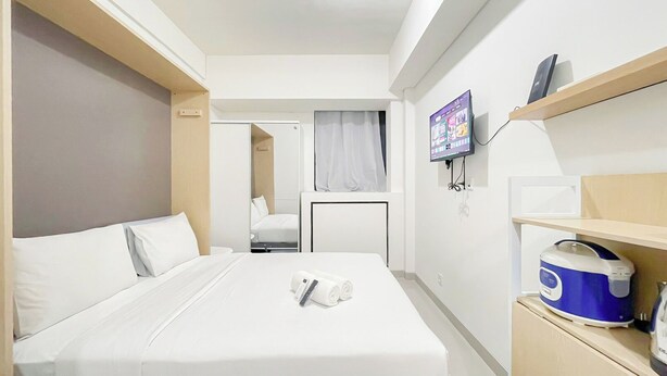 A hotel room with a large bed, a desk, a television, and a microwave on a shelf. - White Studio Room (No Kitchen) At Bandaraya - Tallasa City Makassar Apartment (Makassar)