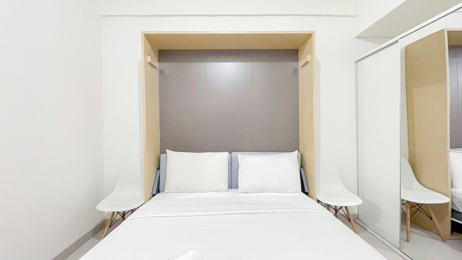 Quarto de hotel moderno com cama, mesa de cabeceira, espelho e armário.