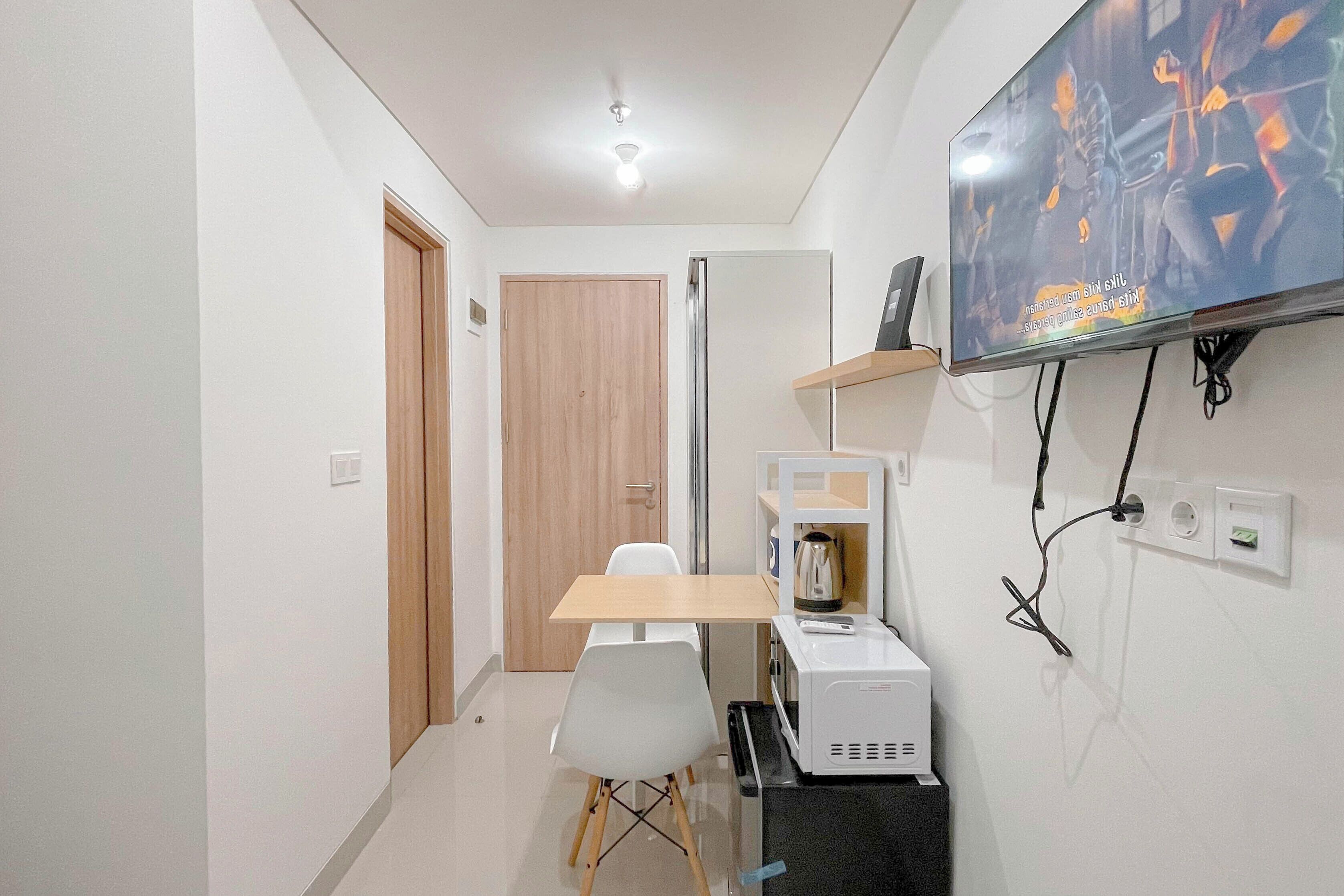 Una stanza moderna e accogliente con una porta in legno, un tavolo bianco con una sedia, un forno a microonde e un televisore fissato al muro.