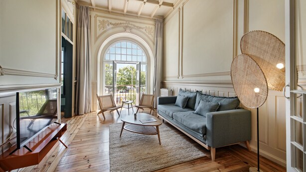A spacious living room with a wooden floor, a grey sofa, a coffee table, and a TV on a wooden stand. - PG - 1C - T1 Superior - Palacete do Guadiana (Vila Real Santo Antonio)