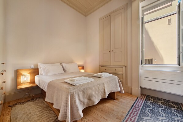 A bedroom with a bed, bedside lamps, a wardrobe, and a window.