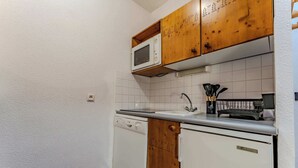 Cocina compacta con gabinetes blancos, microondas, lavaplatos y lavadero.