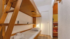 Habitación pequeña con literas, un estante con plantas y un mueble de madera con utensilios de cocina.