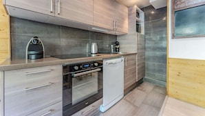A modern kitchen with wooden cabinets, a built-in oven, a dishwasher, and a coffee machine.